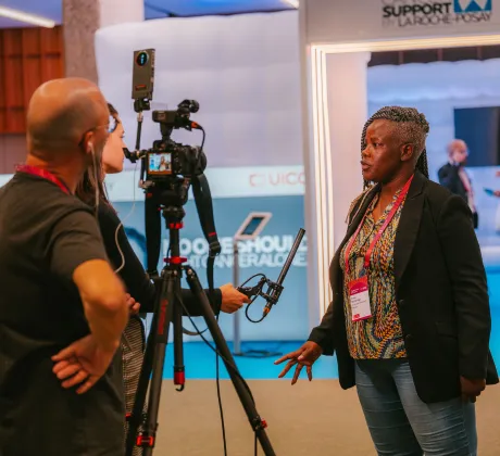 A woman speaking in front of a camera, with a person holding a mic for her