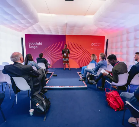 Speaker presenting on the Spotlight Stage at the World Cancer Congress 2024 in Geneva, Switzerland, addressing a seated audience in a small session space with a branded backdrop displaying “Spotlight Stage” and the World Cancer Congress logo.