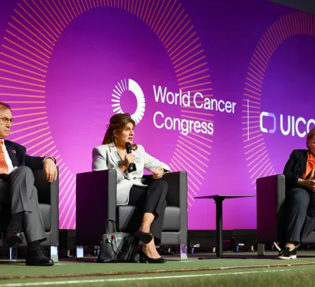 Plenary panel discussion at the World Cancer Congress 2024 in Geneva, Switzerland, showing three speakers seated on a stage with a purple backdrop displaying the World Cancer Congress and UICC logos, as one speaker holds a microphone and addresses the audience.