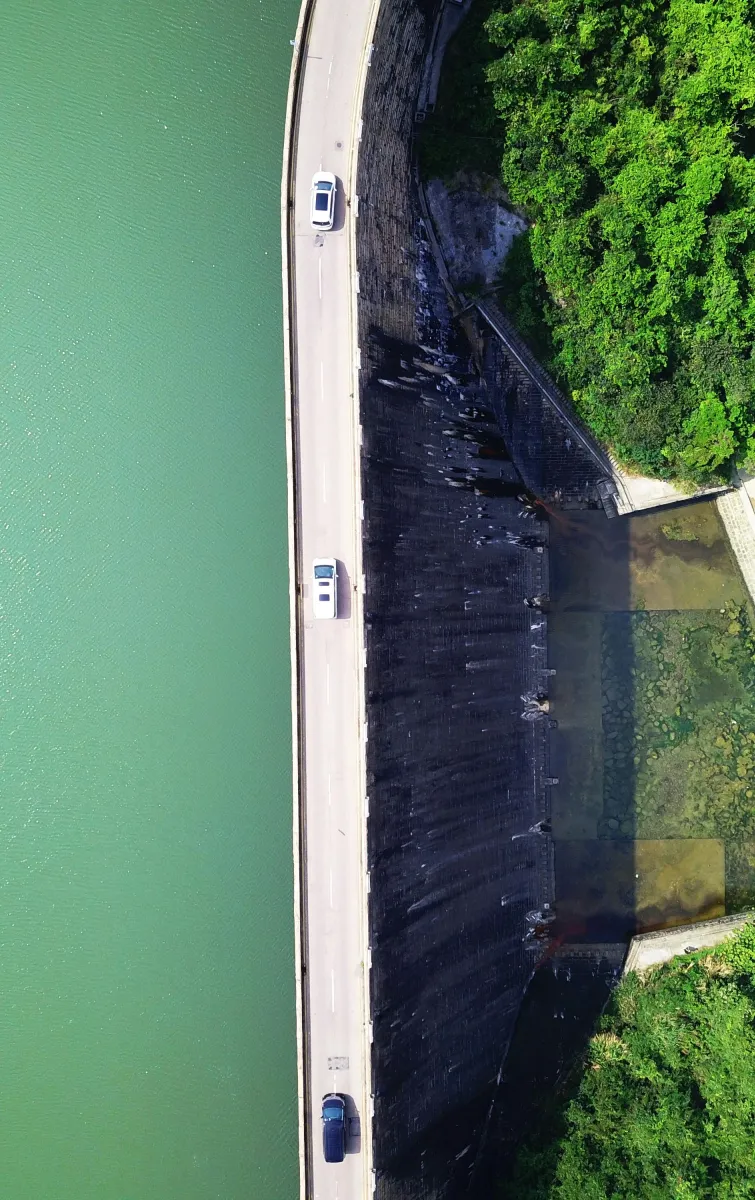 An aerial view of water, a dam with a road on it and forestry.