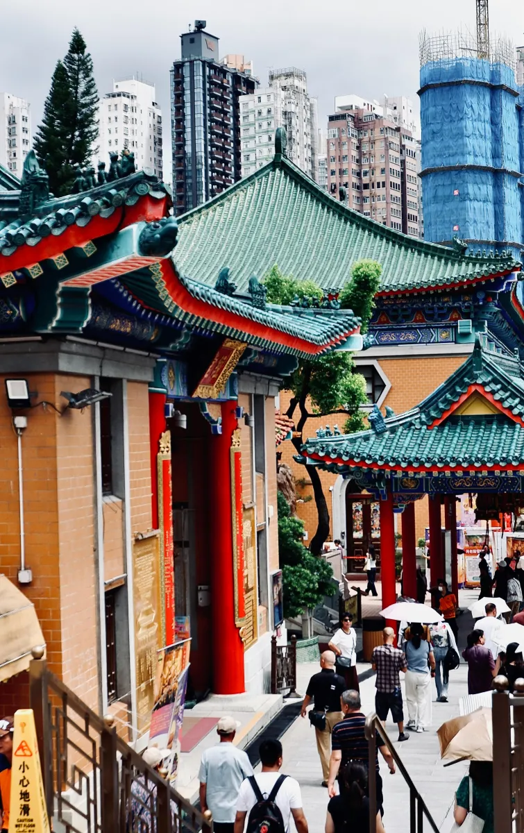 Photo of a traditional building in Hong Kong with people walking in the street, behind we can see skyscrapers